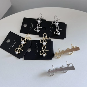 Elegante Haarklammern mit Schleife in Gold und Silber sowie Perlen auf grauem Grund