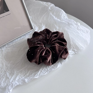 Detail of dark brown velvet scrunchie with sparkling white beads on a textured background