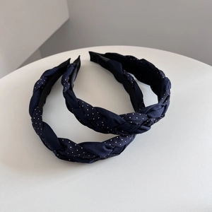 Detail showing two navy blue polka dot braided headbands on a minimalist white stand
