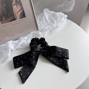 Detail showing a black satin bow scrunchie with white heart patterns and long ribbon tails