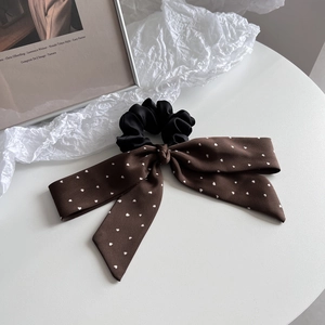 Detail of elegant black satin hair scrunchie with printed ribbon on a minimalist desk