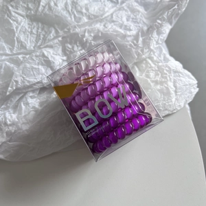Close-up of purple gradient spiral hair ties in a clear box with gold BOW branding