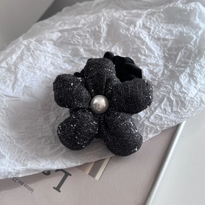 Close-up of a tweed flower hair tie with a glossy pearl center on a white paper background