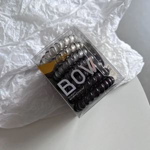 Close-up of nine spiral phone cord hair ties in gradient grey colors inside a clear box