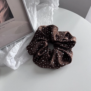 Gros plan d'un grand chouchou en satin marron orné de strass argentés brillants