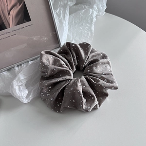 Détail d'un chouchou en satin gris orné de strass sur un fond blanc minimaliste