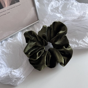 Macro shot of dark green velvet scrunchie showing soft texture and pleated craftsmanship