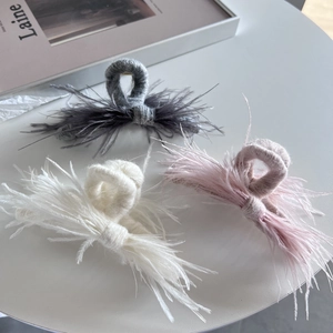 Detail of knit hair clips in grey, white and pink with delicate ostrich feather trim