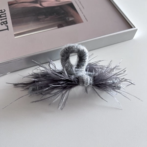 Close-up of grey knitted hair claw clip with ostrich feathers on a leather surface
