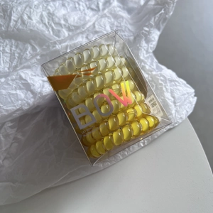 Macro detail of yellow and cream spiral phone cord hair ties in a transparent box