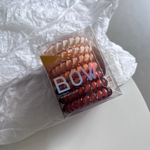 Detailed view of warm brown gradient spiral hair ties in a clear minimalist display box