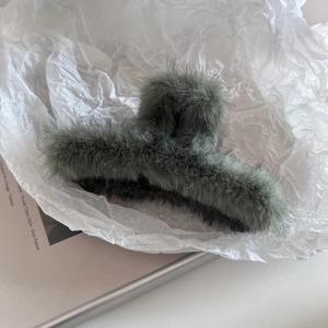 Gros plan d'une grande pince à cheveux en peluche vert foncé sur un magazine minimaliste