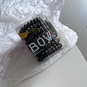 Set of 12 black spiral elastic hair ties in a clear branded box with a laser bow design