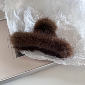 Vue détaillée de la pince à cheveux en fausse fourrure marron foncé sur papier d'art