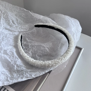 Detail view of the white plush headband with shiny sequins on soft wrinkled paper