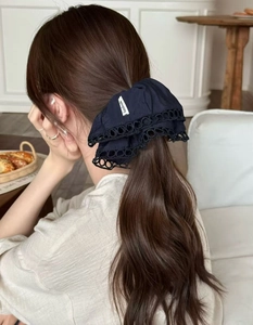 Close-up of black cotton scrunchie with lace edge and handmade label on a wooden table