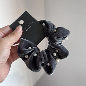 Close-up of a dark grey velvet scrunchie with white pearl accents and product tag