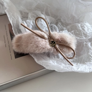 Détail d'une pince à cheveux en peluche abricot avec nœud en cuir et pendentif doré
