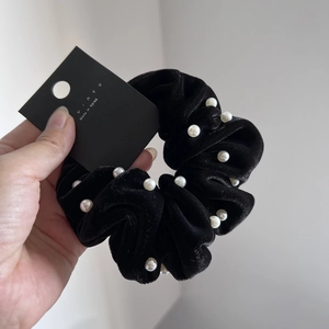 Close-up of black velvet scrunchie with white pearls on a minimalist brand card
