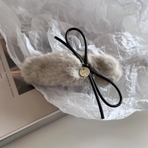 Détail d'une pince à cheveux en peluche grise avec nœud en cuir et pendentif doré