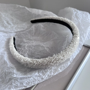 Close-up of white tweed padded headband with sequins on textured tissue paper