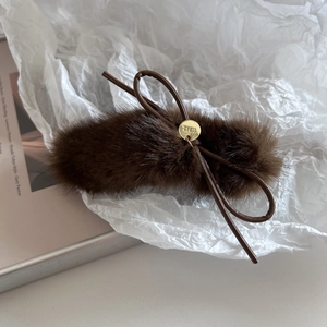 Gros plan sur la pince à cheveux en peluche marron avec nœud doux et pendentif doré