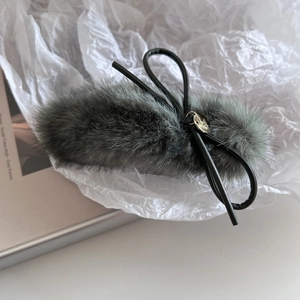 Détail de la pince à cheveux en peluche grise avec nœud noir et pendentif doré