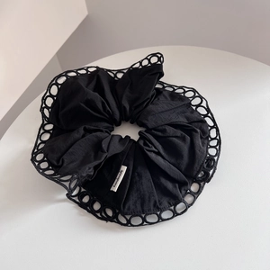 Detailed view of black fabric scrunchie with hollow lace edges and handmade tag