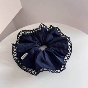 Close-up of navy blue scrunchie with lace trim and handmade label on white pedestal