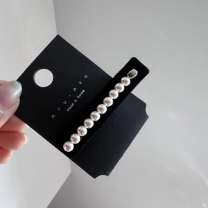 Détail de 11 perles blanches polies sur un clip en métal argenté sur carte de marque