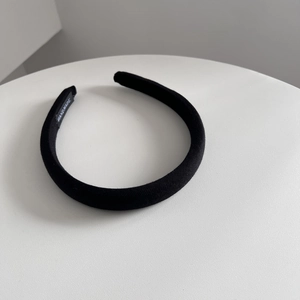 Close-up of black fabric padded headband with a handmade label on white pedestal