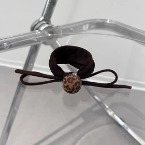 Close-up of brown suede bow hair tie with leopard print bead detail on a modern stand