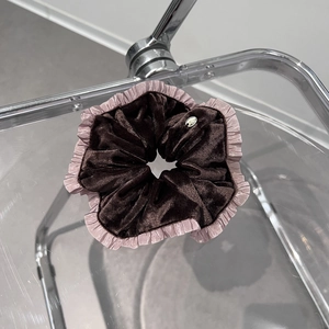 Détail d'un chouchou en velours marron avec bordure rose à volants et badge métal