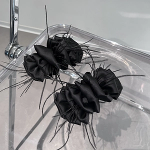 Elegant pair of black satin flower hair clips with decorative feathers on a modern chair