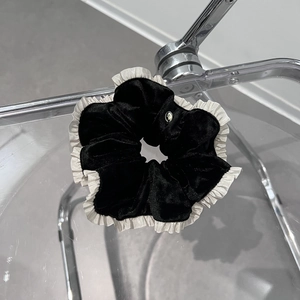 Détail du chouchou en velours noir avec bords blancs volantés et médaillon argenté