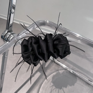 Detail view of black feather hair clip with pleated satin texture on display stand