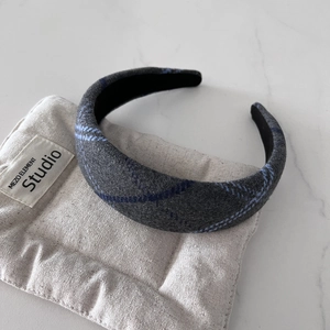 Detail of grey tweed headband with blue plaid texture on a soft cushion display