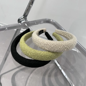 Three padded tweed headbands in black, green, and beige colors on a modern glass display
