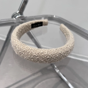 Close-up of beige woven padded headband with handmade label on acrylic stand