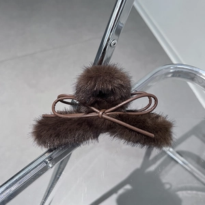 Dettaglio di un mollettone in peluche marrone con fiocco in pelle su metallo argentato