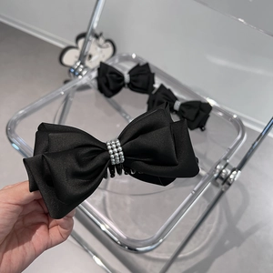 Detail of elegant black satin bow hair clip with three rows of white faux pearls