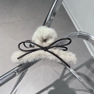 Dettaglio di un grande fermaglio per capelli in peluche beige con fiocco nero