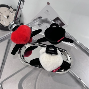 Trois pinces à cheveux cœur en peluche avec ailes en rouge, noir et blanc sur plateau