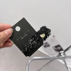 Close-up of black and white tweed hair claw clip with bow detail on a branded card