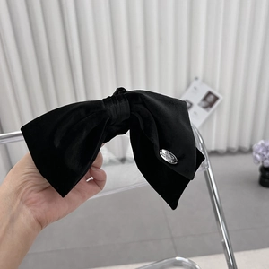 Macro detail of large black velvet bow hair clip with silver logo metal plaque