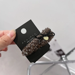 Detail of a brown tweed bow hair claw clip with gold pendant on a display card