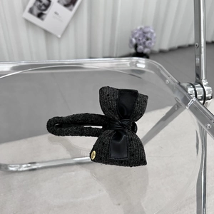 Close-up of elegant black tweed bow hair clip with gold metal tag and premium fabric texture