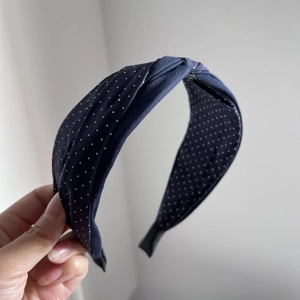 Detail of twist knot navy blue fabric headband with white polka dots held by hand
