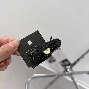 Detail of a black knitted bow hair claw with a gold metal emblem on brand card
