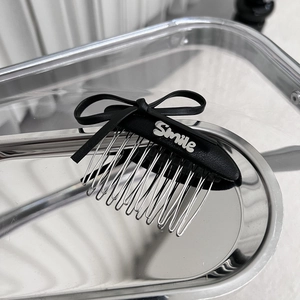 Détail d'un peigne à cheveux avec nœud en cuir noir et plaque Smile argentée sur plateau